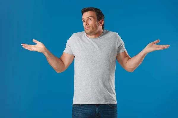 Dudoso hombre haciendo gestos con las manos y mirando hacia otro lado aislado en azul - foto de stock