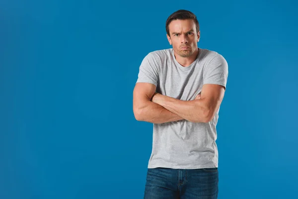 Frowning man standing with crossed arms and looking at camera isolated on blue — Stock Photo