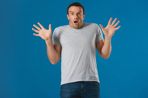 Shocked man raising hands and looking at camera isolated on blue — Stock Photo