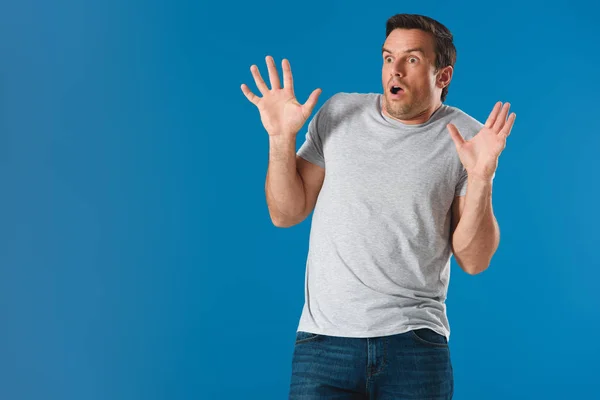 Shocked man raising hands and looking away isolated on blue — Stock Photo