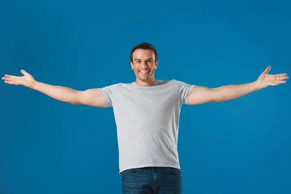 Uomo allegro in piedi con le braccia aperte e sorridente alla fotocamera isolato su blu — Foto stock