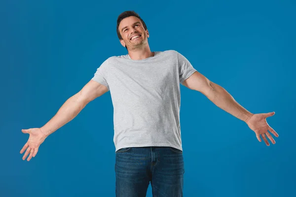Hombre feliz de pie con los brazos abiertos y mirando hacia arriba aislado en azul - foto de stock