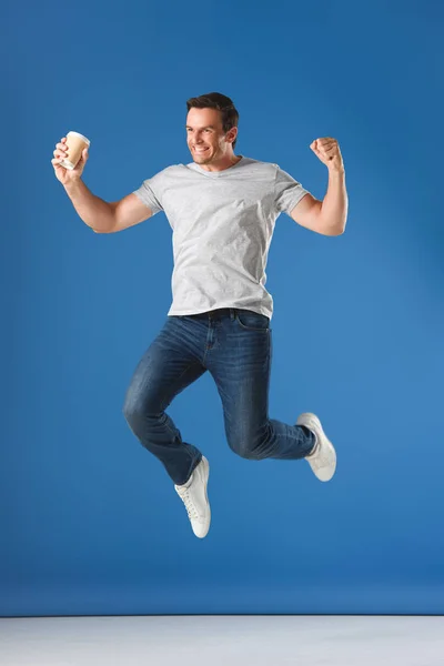 Excited man with coffee to go jumping and triumphing on blue — Stock Photo