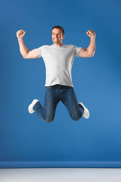Excited man jumping and triumphing on blue — Stock Photo
