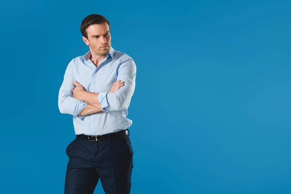 Serious man standing with crossed arms and looking away isolated on blue — Stock Photo