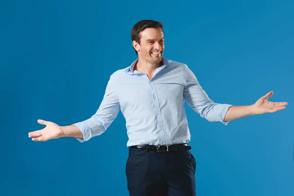 Hombre guapo feliz de pie con los brazos abiertos y mirando hacia otro lado aislado en azul - foto de stock