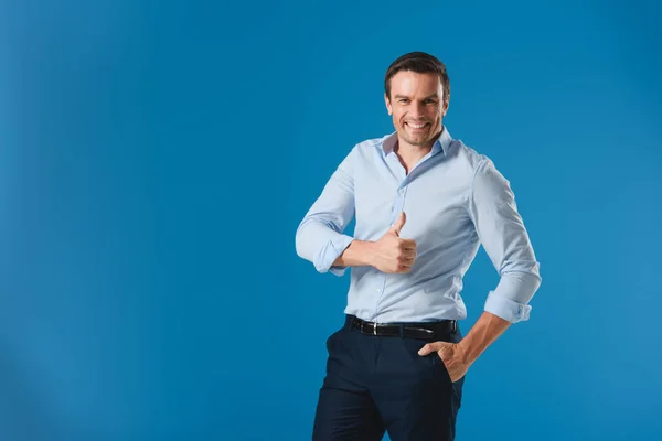 Homem de negócios bonito mostrando polegar para cima e sorrindo para a câmera isolada em azul — Fotografia de Stock