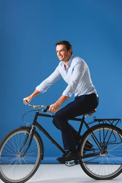 Усміхнений бізнесмен їде на велосипеді і дивиться в сторону на синій — стокове фото