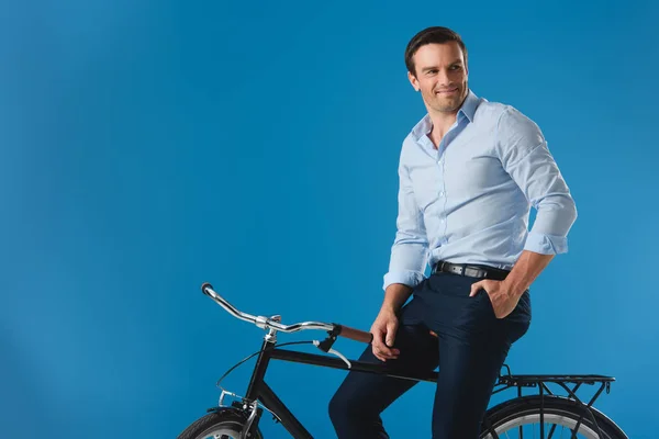 Bel homme souriant assis sur le vélo et regardant loin isolé sur bleu — Photo de stock