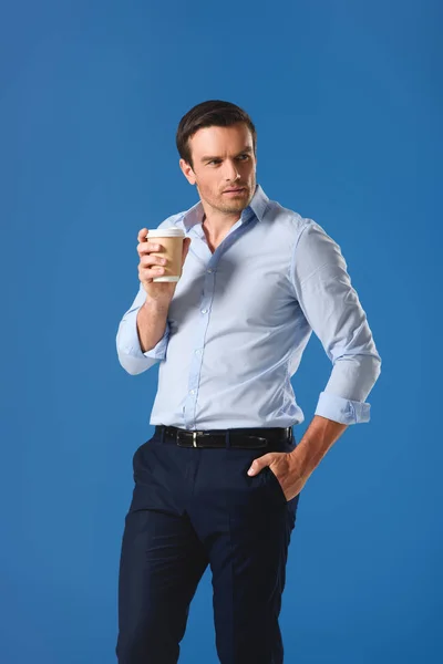 Homem bonito segurando copo de café descartável e olhando para longe isolado em azul — Fotografia de Stock
