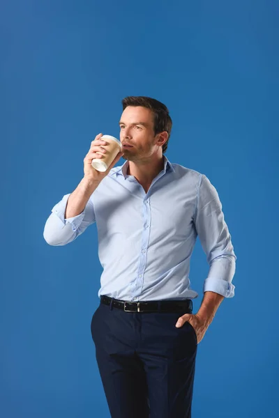 Красивий чоловік п'є з паперової чашки і дивиться ізольовано на синій — стокове фото