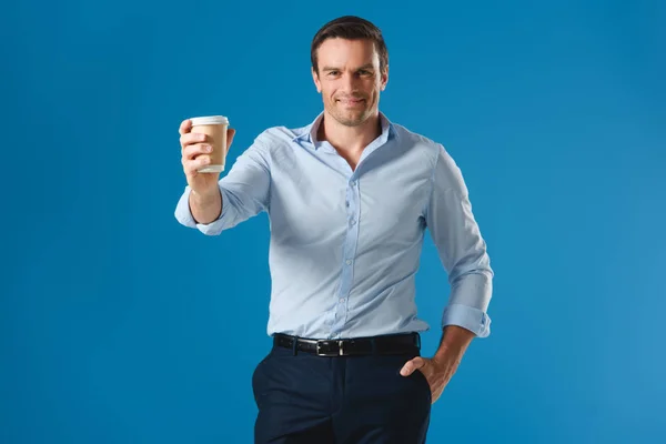 Hombre guapo sosteniendo taza de café desechable y sonriendo a la cámara aislado en azul - foto de stock