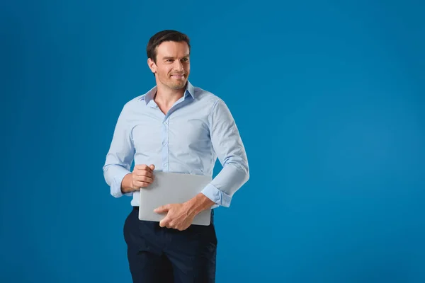 Bel homme souriant tenant ordinateur portable et regardant loin isolé sur bleu — Photo de stock