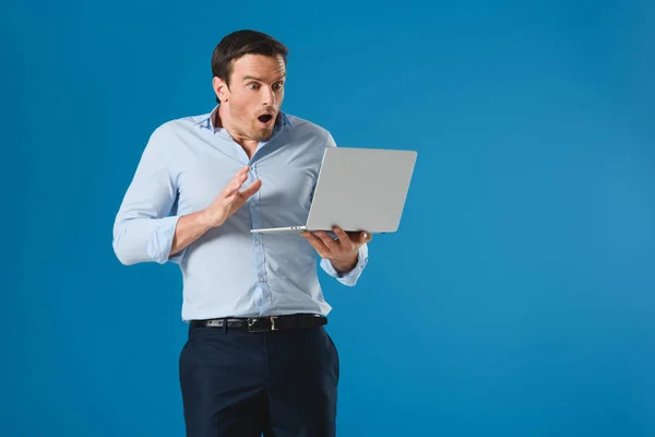 Homme choqué tenant et utilisant ordinateur portable isolé sur bleu — Photo de stock