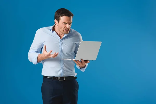 Angry man holding and using laptop isolated on blue — Stock Photo