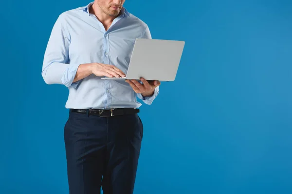 Обрезанный снимок красивого мужчины, держащего и использующего ноутбук изолированный на голубом — стоковое фото