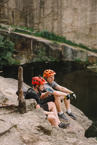Sportsmen in protective helmets resting with apple and sport bottle of water on rocky cliff — Stock Photo