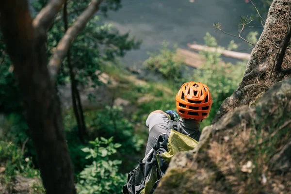 Rückansicht eines männlichen Wanderers mit Schutzhelm, der auf einer Felswand im Wald steht — Stockfoto