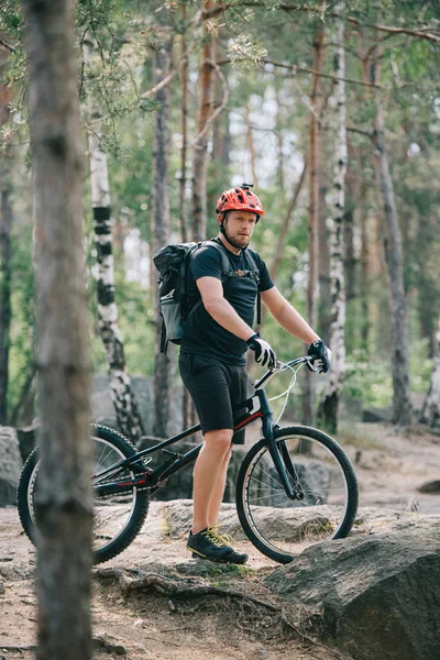 Young male extreme cyclist in protective helmet standing with mountain bicycle in forest — Stock Photo