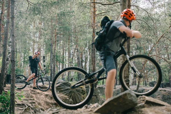 Ciclista extremo masculino en bicicleta de montaña mostrando el gesto de pulgar hacia arriba a un amigo con bmx en el bosque - foto de stock