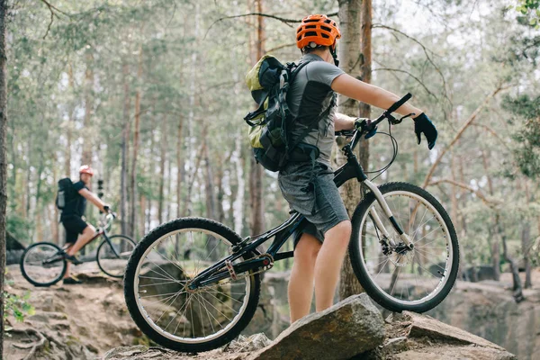 Selective focus of male extreme cyclist on mountain bike talking to friend with bmx in forest — Stock Photo