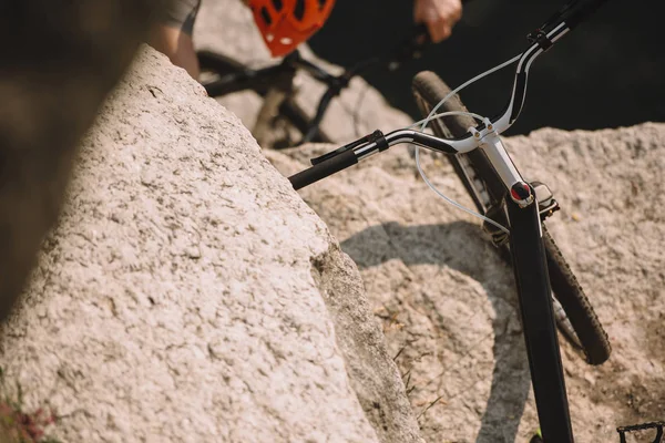 Foco seletivo da bicicleta de montanha na rocha e ciclista extremo masculino no capacete andando de bicicleta atrás — Fotografia de Stock