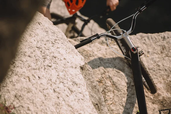 Selective focus of mountain bike on rock and male extreme cyclist in helmet riding on bicycle behind — Stock Photo