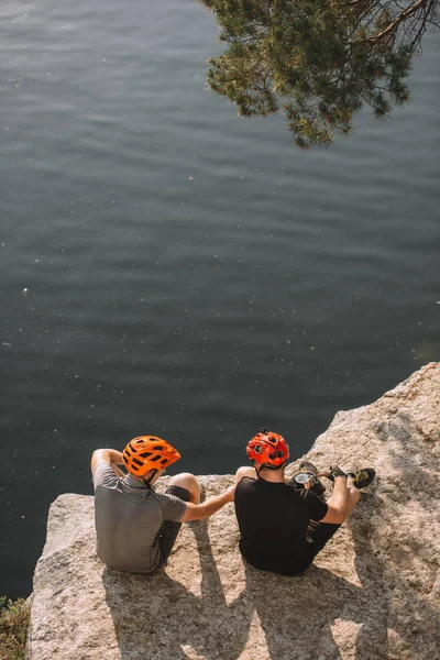 High angle view of male hikers in protective helmets eating canned food on rocky cliff over river — Stock Photo