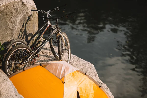 Vista de ángulo alto de bicicletas de montaña y tienda de campaña en acantilado rocoso sobre el río - foto de stock