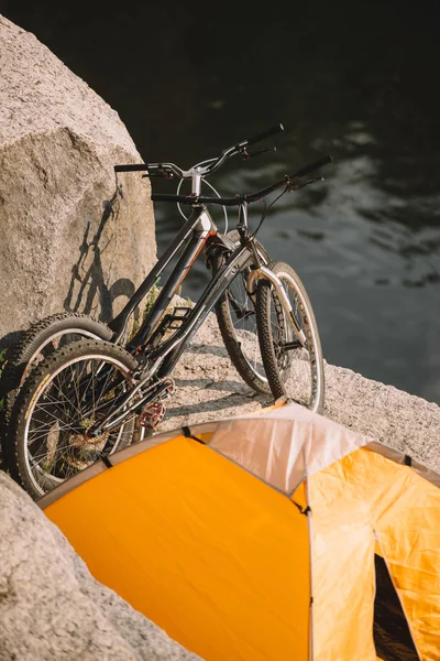 Vue panoramique de deux vélos de montagne et tente touristique sur une falaise rocheuse surplombant la rivière — Photo de stock