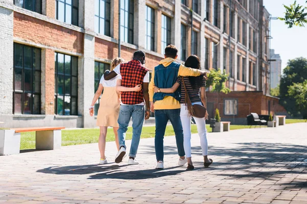 Vue arrière d'un groupe multiculturel d'amis qui se câlinent en marchant ensemble dans la rue — Photo de stock