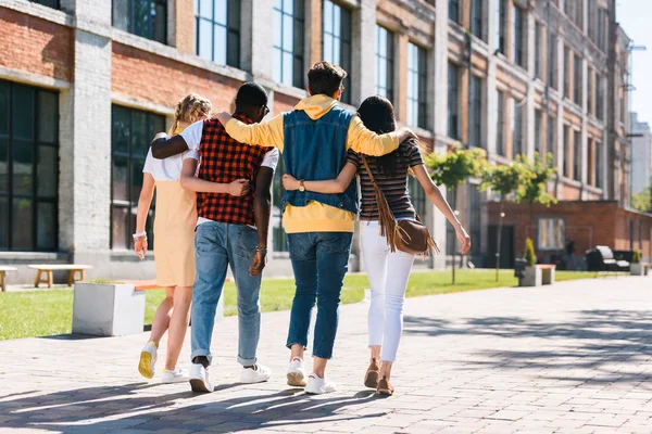 Back view of multicultural group of friends hugging while walking on street together — Stock Photo