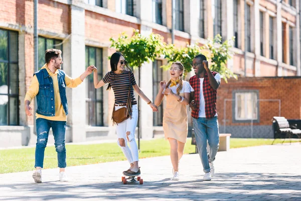 Happy multiracial friends with long board having fun while spending time together on street — Stock Photo