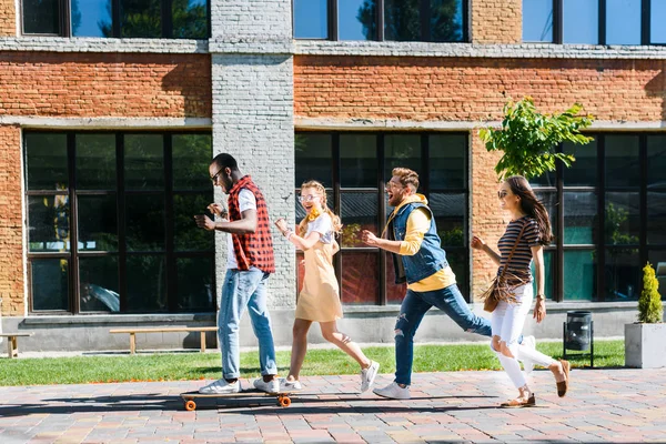 Happy multiracial friends with long board having fun while spending time together on street — Stock Photo