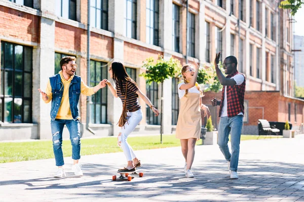 Happy multiracial friends with long board having fun while spending time together on street — Stock Photo