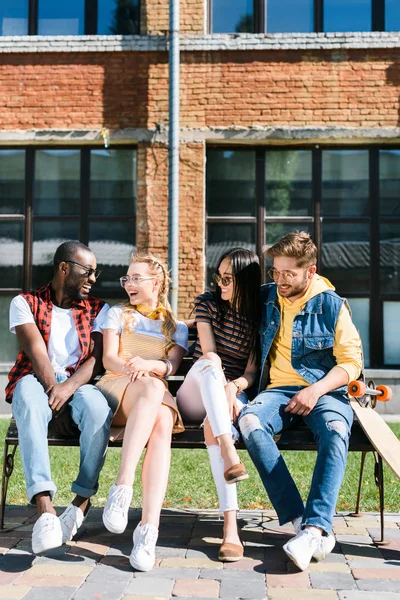 Couples multiculturels joyeux reposant sur un banc ensemble dans la rue — Photo de stock