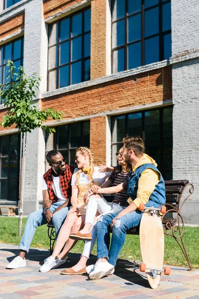 Couples multiculturels joyeux reposant sur un banc ensemble dans la rue — Photo de stock