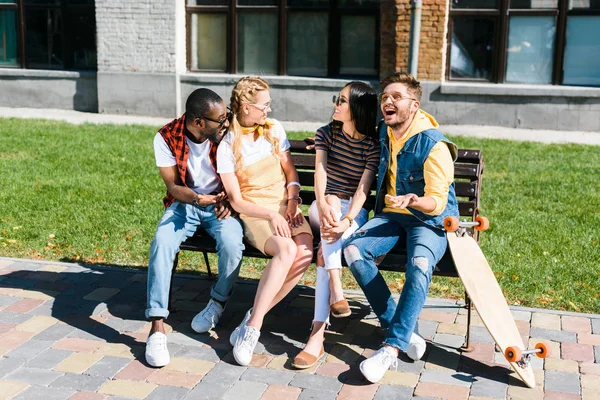 Couples multiculturels joyeux reposant sur un banc ensemble dans la rue — Photo de stock