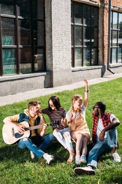 Gruppo interrazziale di amici con chitarra acustica a riposo su erba verde nella giornata estiva — Foto stock