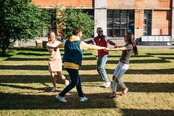 Amigos jóvenes multiculturales tomados de la mano mientras se divierten juntos en el día de verano - foto de stock