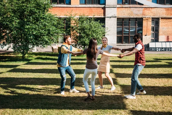 Amigos jóvenes multiculturales tomados de la mano mientras se divierten juntos en el día de verano - foto de stock