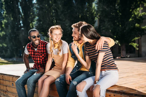 Multicultural cheerful couples sitting on wooden parapet together — Stock Photo