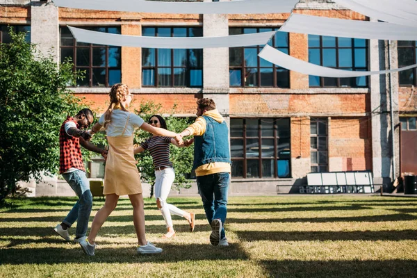 Amigos jóvenes multiculturales tomados de la mano mientras se divierten juntos en el día de verano - foto de stock