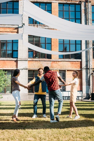 Мультикультурные молодые друзья держатся за руки, веселясь вместе в летний день — стоковое фото