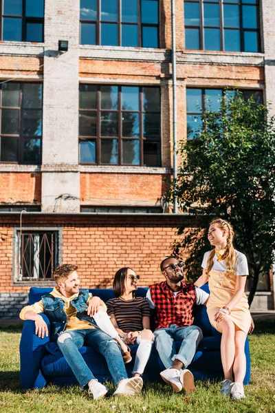 Sorrindo amigos inter-raciais descansando no sofá azul juntos — Fotografia de Stock