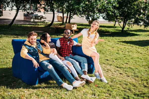Sorridenti amici interrazziale riposano sul divano blu insieme nel parco — Foto stock