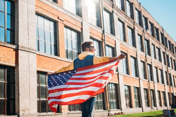 Back view of young man with american flag in hands on street — Stock Photo