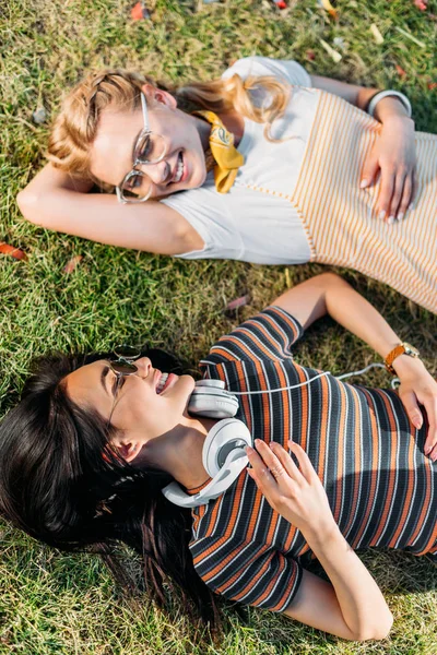 Мультикультурні молоді усміхнені жінки відпочивають на зеленій траві в парку — Stock Photo