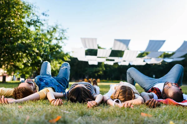 Межрасовые друзья отдыхают на зеленой лужайке в парке вместе — стоковое фото