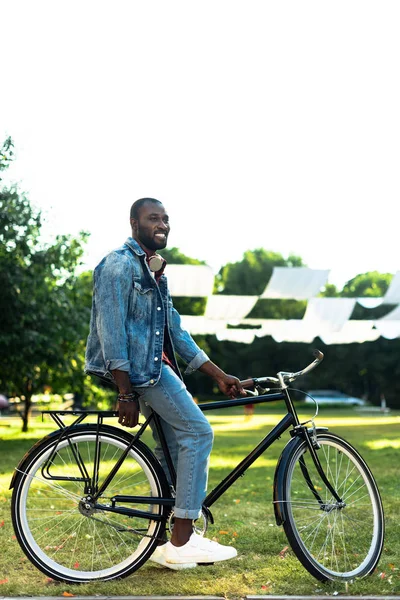 Vista lateral del hombre afroamericano sonriente con bicicleta retro en el parque - foto de stock